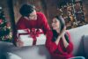Χριστουγεννιάτικα δώρα για γυναίκες – ένας άντρας δίνει ένα δώρο σε μια γυναίκα, και οι δύο φορούν κόκκινα πουλόβερ, μια γιορτινή ατμόσφαιρα τριγύρω