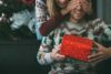 ιδέες για χριστουγεννιάτικα δώρα για άνδρες - μια γυναίκα δίνει δώρο στον άνδρα, και οι δύο φορούν γιορτινά πουλόβερ