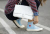 γυναίκα με λευκή τσάντα δένει κορδόνια στα μπλε sneakers της