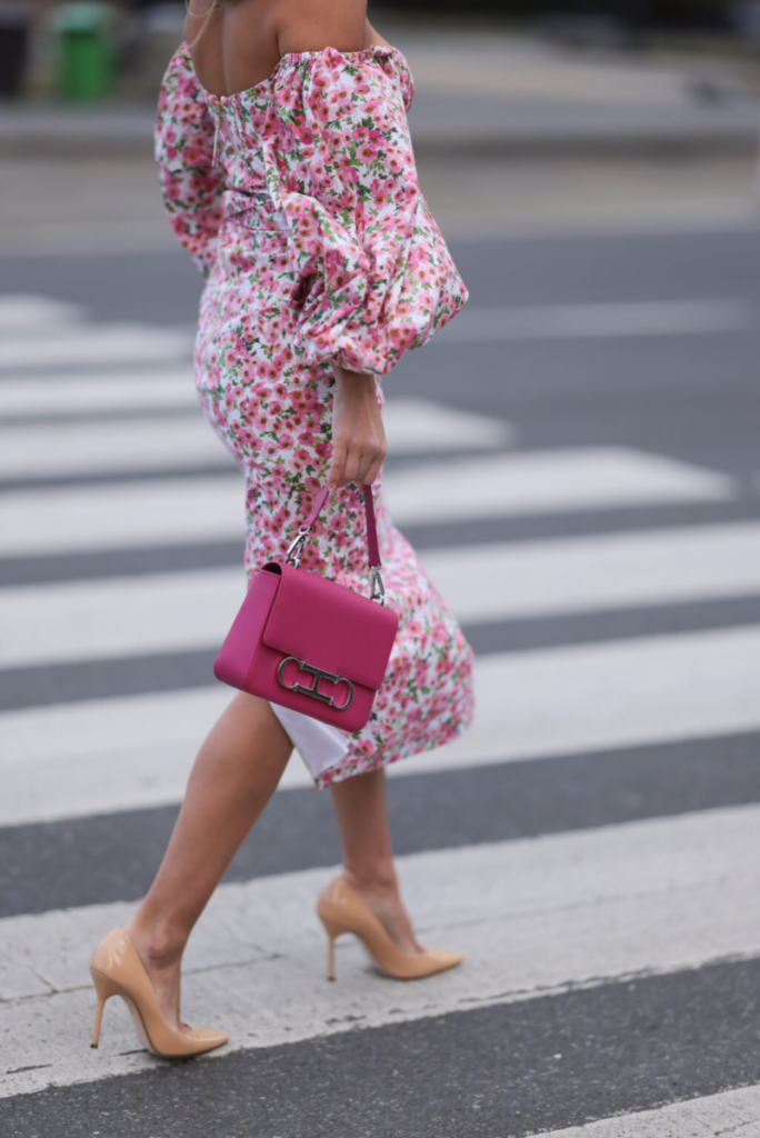 Γυναίκα με φλοράλ φόρεμα με φουσκωτά μανίκια που αποκαλύπτουν τους ώμους με τσάντα σε έντονο ροζ χρώμα και μπεζ βερνικωμένες γόβες στιλέτο